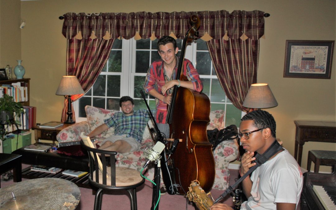 Young man standing with string bass with two others on couch