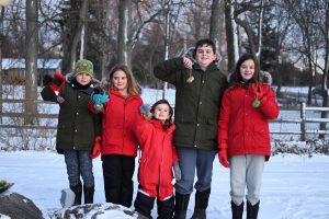 5 children in snow clothes holding up bird feeders in snow